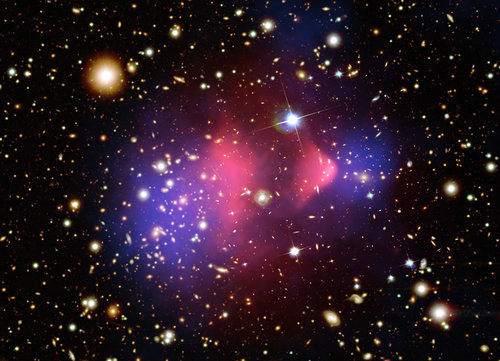 Esta imagen compuesta muestra el cúmulo de galaxias 1E 0657­56, formado después de la colisión de dos grandes conglomerados de galaxias. El gas caliente detectado por el telescopio de rayos X “Chandra”, representado por el color rosado, contiene la mayor parte de la materia ordinaria. Las regiones en azul muestran donde debería estar la mayor parte de la masa según efectos gravitacionales (usando la técnica de los lentes gravitacionales). La mayoría de la materia, en el lado azulado, está claramente separada de la ordinaria (región rosada) y no es observable directamente. La mejor explicación de la que se dispone es que allí hay Materia Oscura. Imagen cortesía: Colaboración Chandra, Universidad de Harvard.
